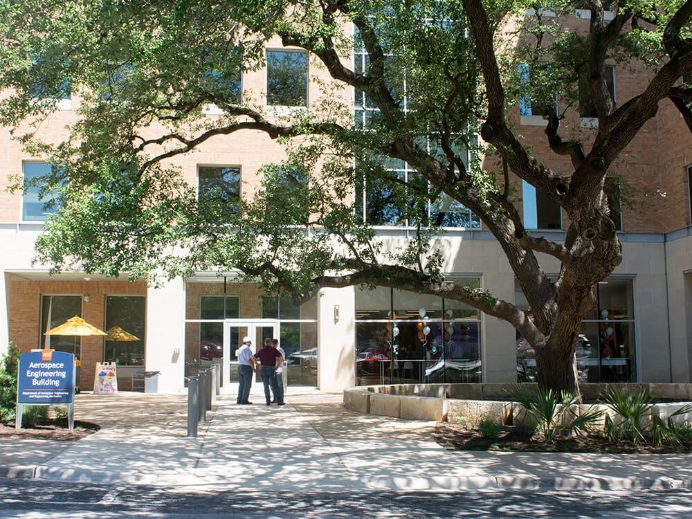 three men talking in front of the doors to the Aerospace Engineering Building at UT Austin
