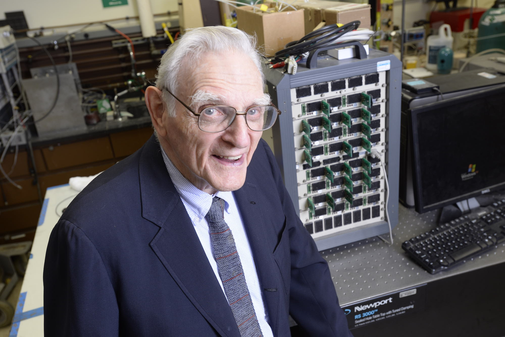 Portrait of John Goodenough in the lab standing in front of some of his equipment