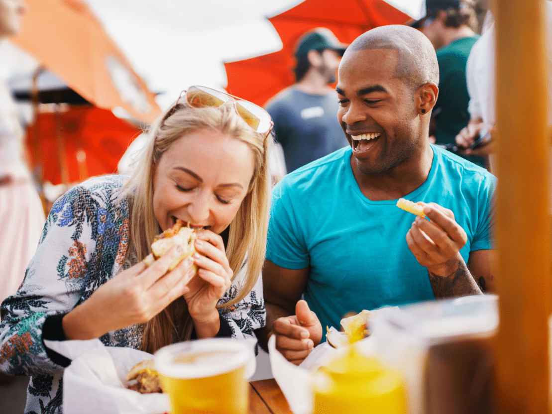 Man and woman smiling while eating sanwiches
