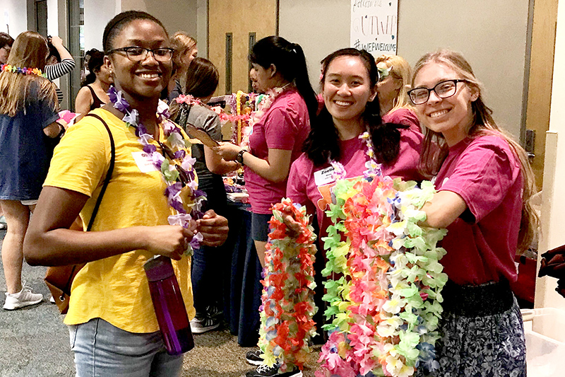 Three Tx engineering students handing out leis at UT Austin Women in Engineering Welcome Event