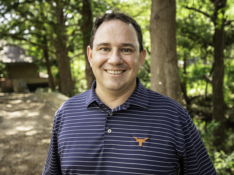 Michael Webber smiling in front of a forest wearing a UT Austin polo