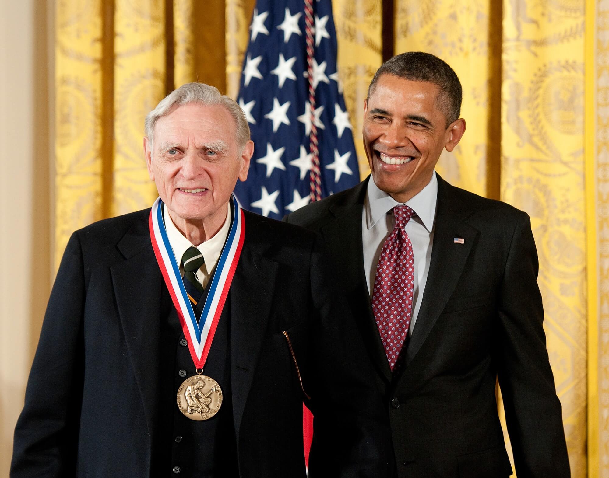 John Goodneough smiling with the National Medal around his neck alongside former President Barack Obama