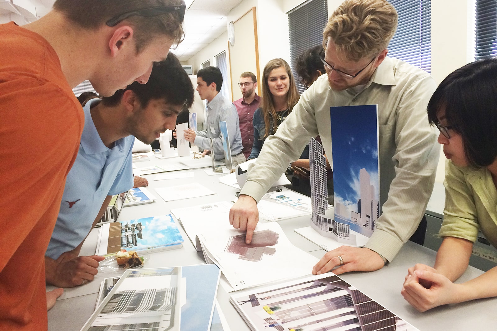 Texas architectural engineering students gathered around a table while professor gestures to book